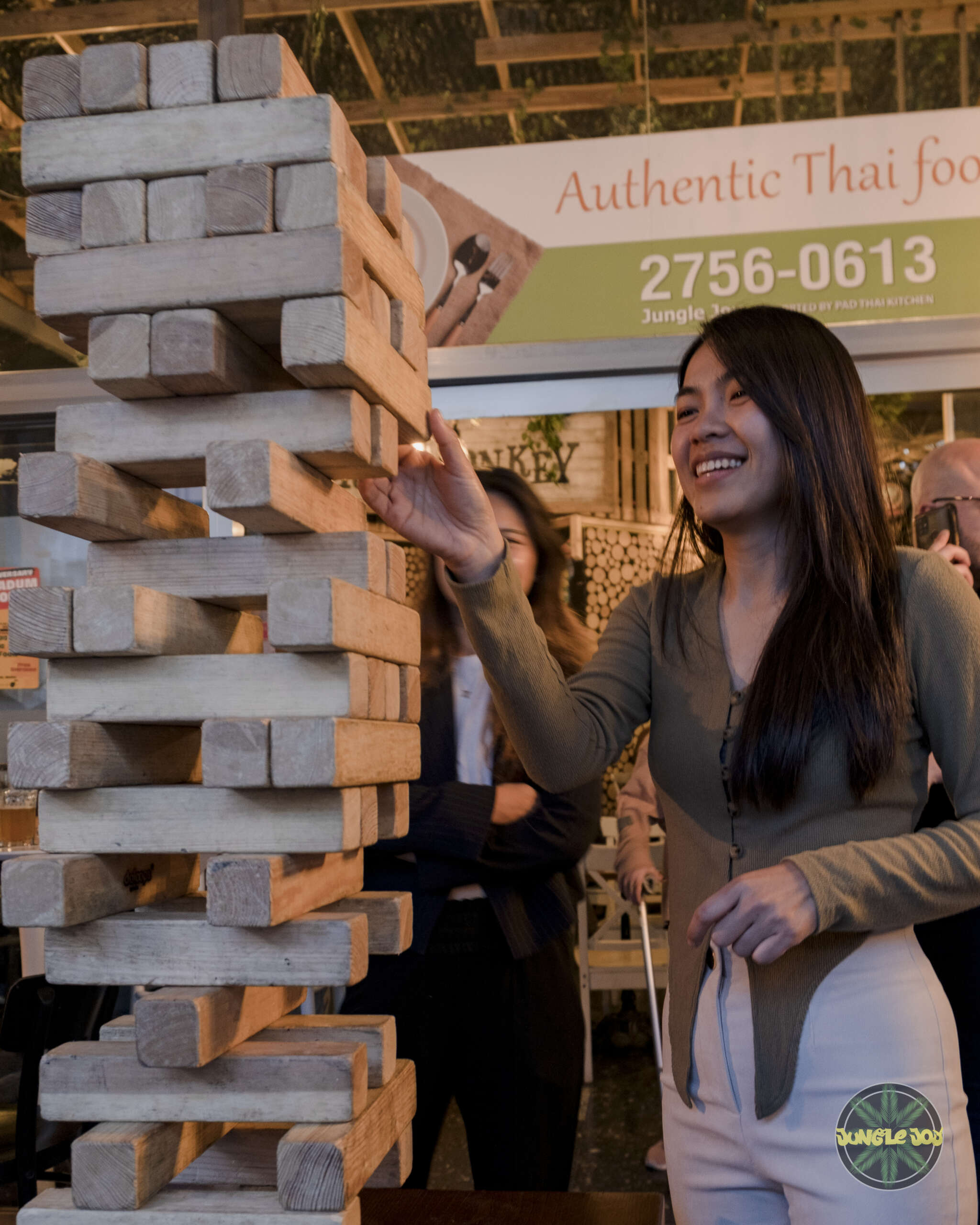 Joyful Moment: Smiling Girl Engrossed in Playing Giant Jenga, Radiating Happiness and Fun